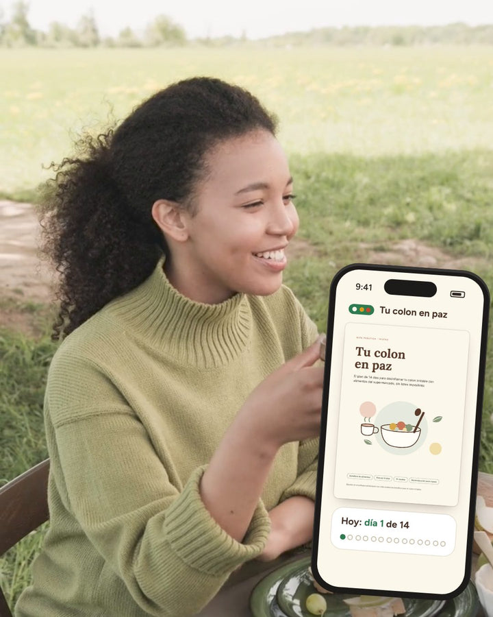 Mujer sonriendo en un almuerzo al aire libre, con el plan de 14 días Tu colon en paz en su celular